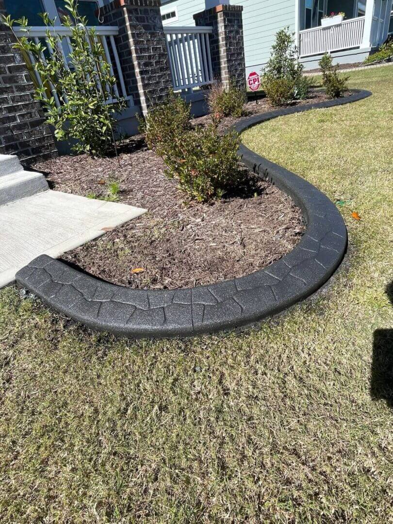 Black stamped concrete landscape curbing around a front planting bed in Hampton Roads